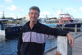 He stands at the Esperance boat harbour, with boats behind him