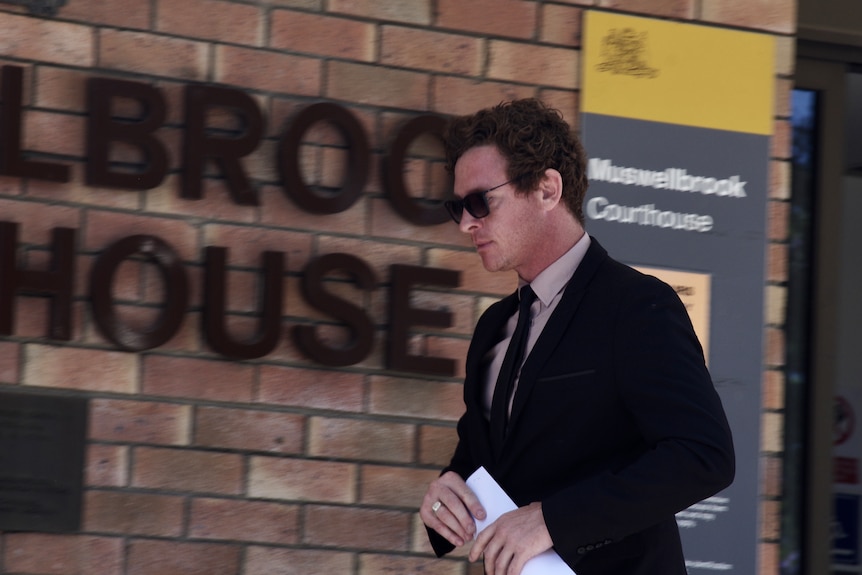 A man in a suit and sunglasses walks away from court.