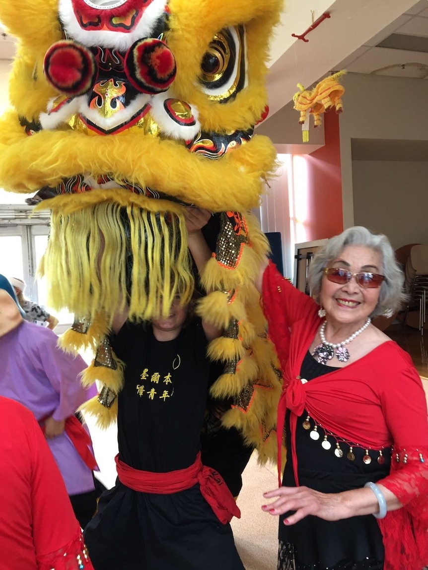 A picture of a Chinese woman with grey hair smiling next to a Chinese dragon.