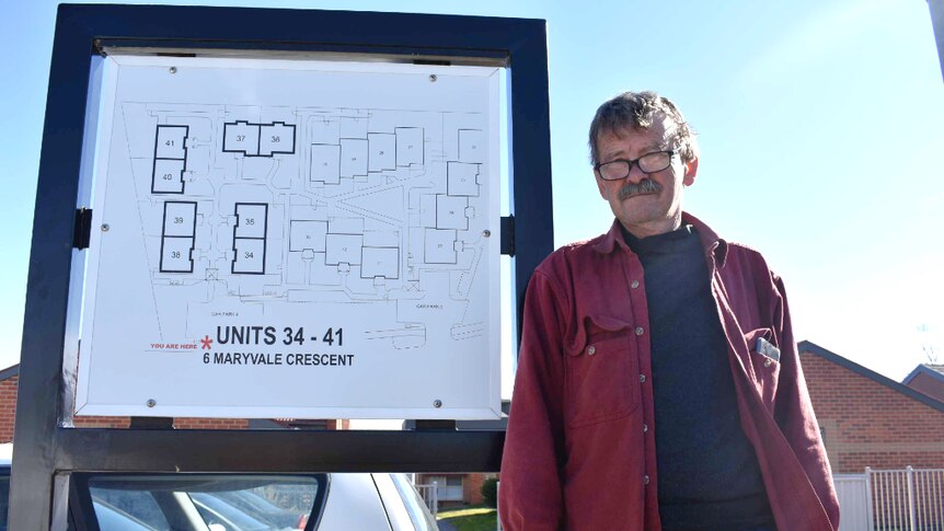 A man stands outside his Morwell apartment leaning against a map of the units