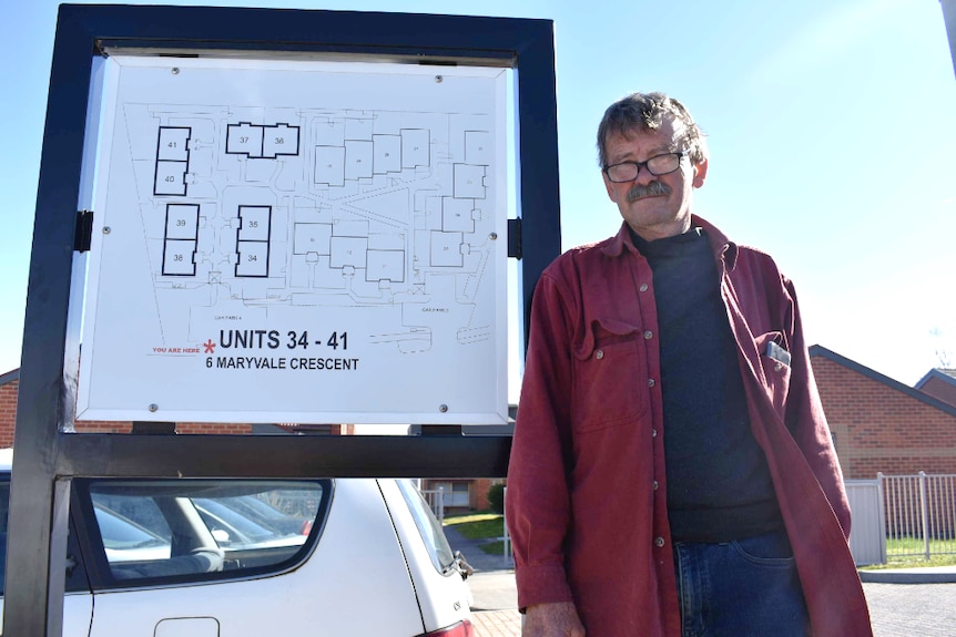 A man stands outside his Morwell apartment leaning against a map of the units