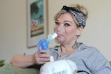 Cassandra Smith sits in her loungeroom wearing a nebuliser mask