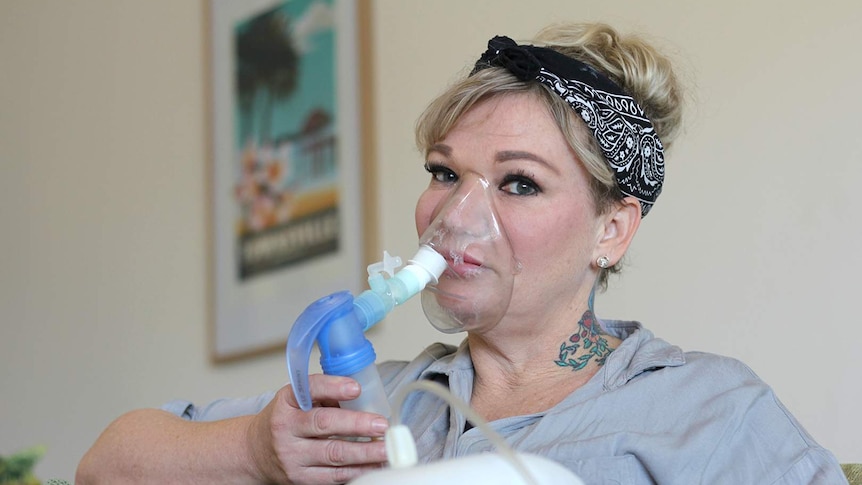 Cassandra Smith sits in her loungeroom wearing a nebuliser mask