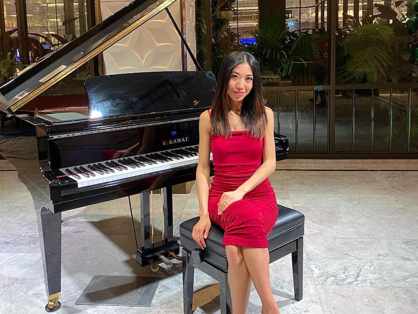 A young women wearing a red dress sits in front of a grand piano.
