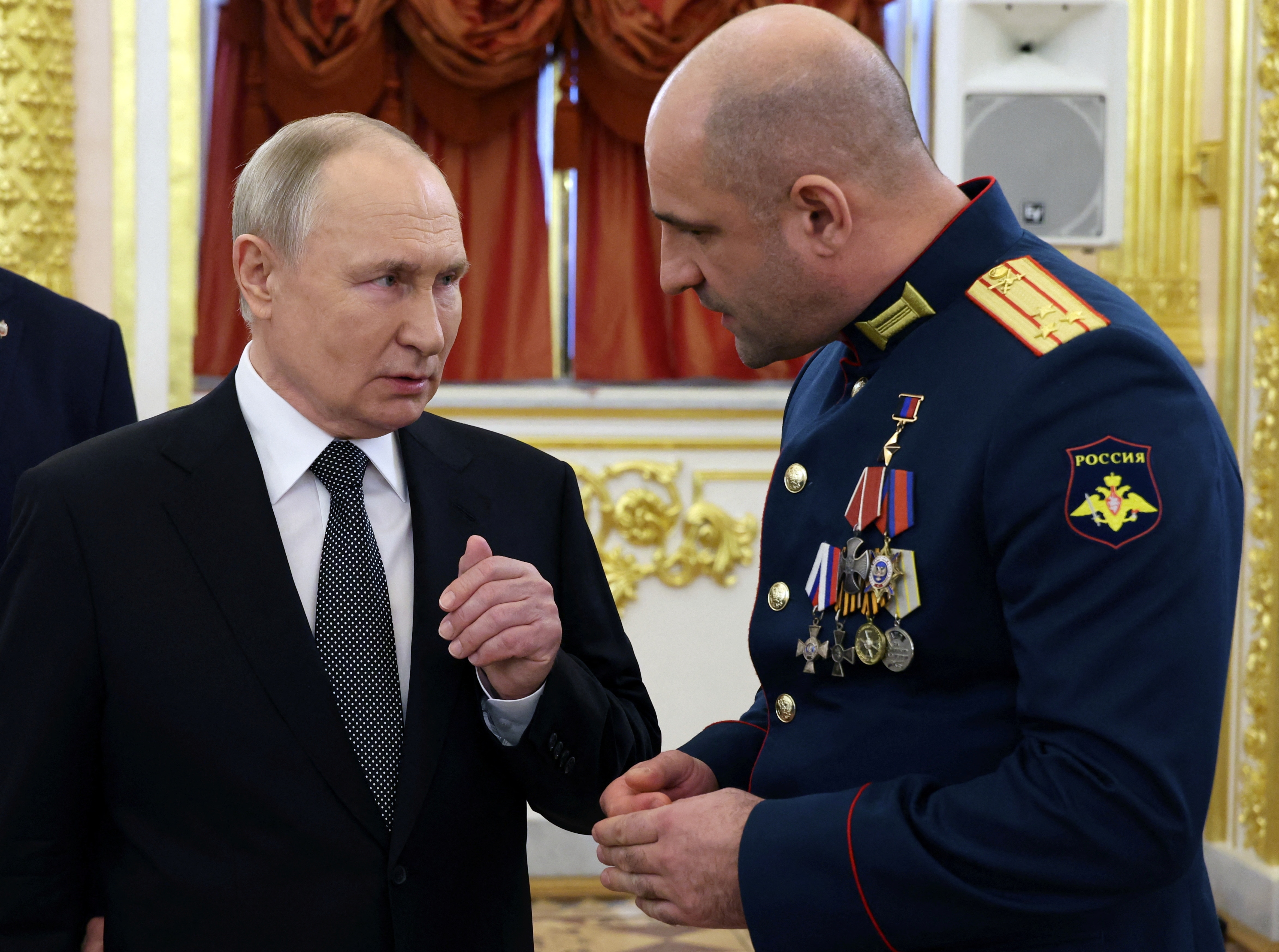 A man in a suit speaking to a man in military uniform, in a ballroom during a ceremony