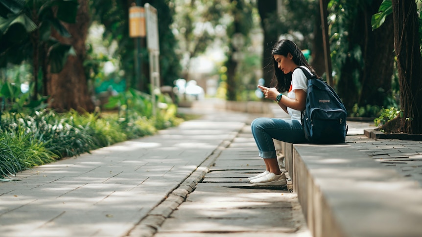 A Woman sits on a bench checking her phone