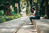 A Woman sits on a bench checking her phone