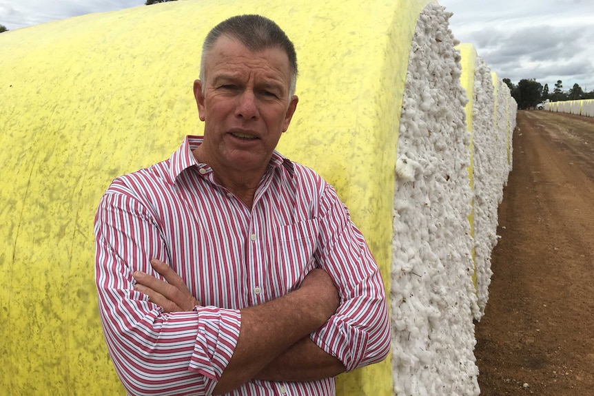 A man stands with his arms crossed in front of a bale of cotton
