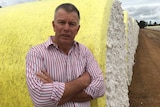 A man stands with his arms crossed in front of a bale of cotton