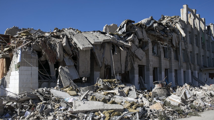 The rubble of a destroyed brick building next to a road with blue sky behind