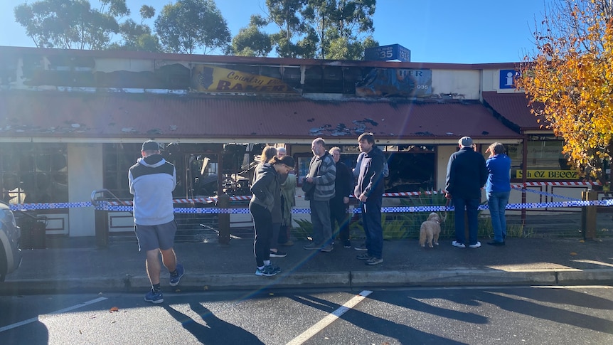 People gather outside burnt-out shops in a car park