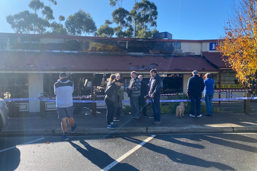 People gather outside burnt-out shops in a car park