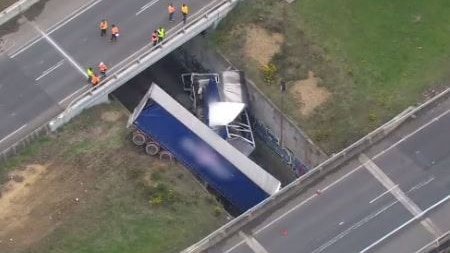 Aerial view of crashed truck smashed onto railway tracks between two overpass highway lanes.