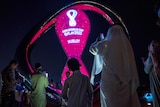 people in traditional arab dress take photos of countdown fifa clock