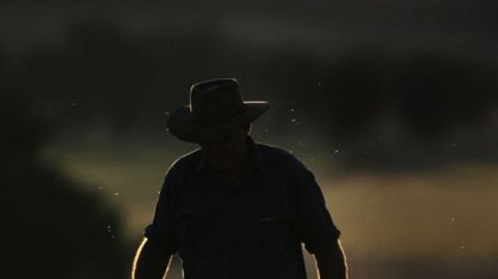 A man with a hat in silouhette, kicking up dust as he walks through a field