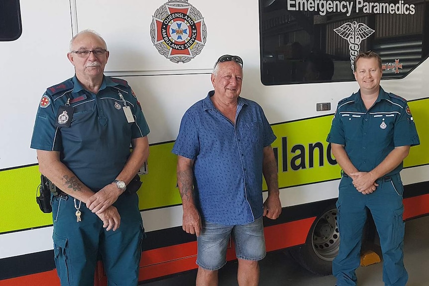 A man stands smiling between two ambulance paramedics