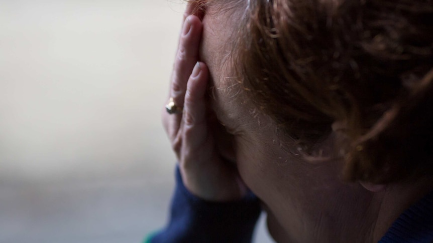 A close-up shot of a woman (unidentified) with her head in her hands