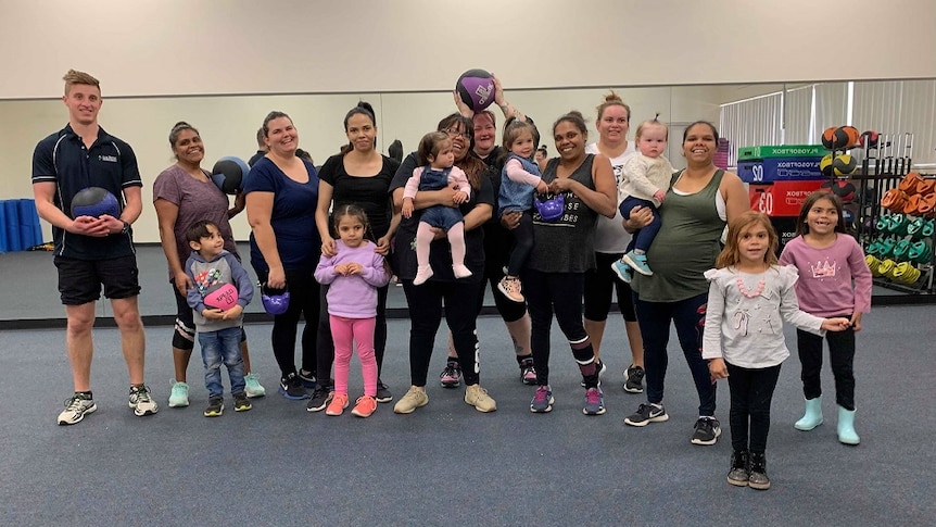 A number of women and children and a man are standing in a group, smiling at the camera. Some are holding exercise equipment.