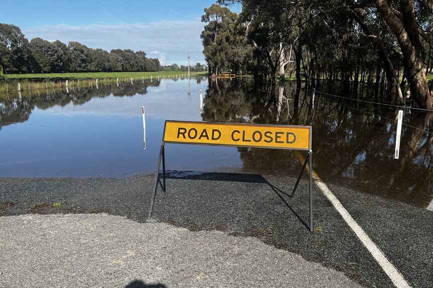 A road clsoed sign in front of a flooded road on a clear blue day.