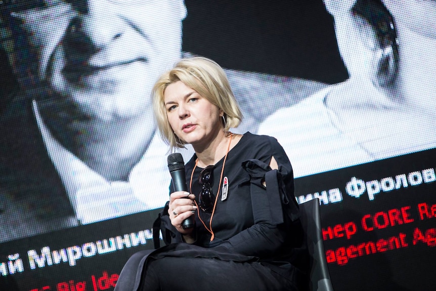 A woman wearing black holds a microphone.