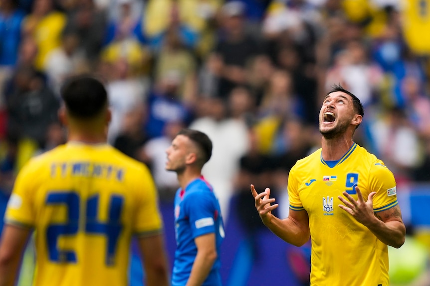 A Ukrainian footballer shouts and looks to the sky in celebration after scoring a late winner in a EURO 2024 game.