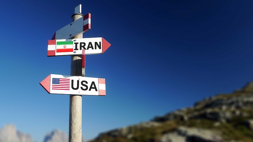 A wooden post with two signs on it pointing in opposite directions. One says Iran and the other says USA.