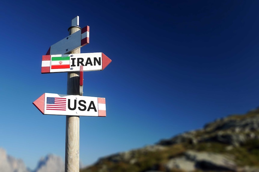 A wooden post with two signs on it pointing in opposite directions. One says Iran and the other says USA.