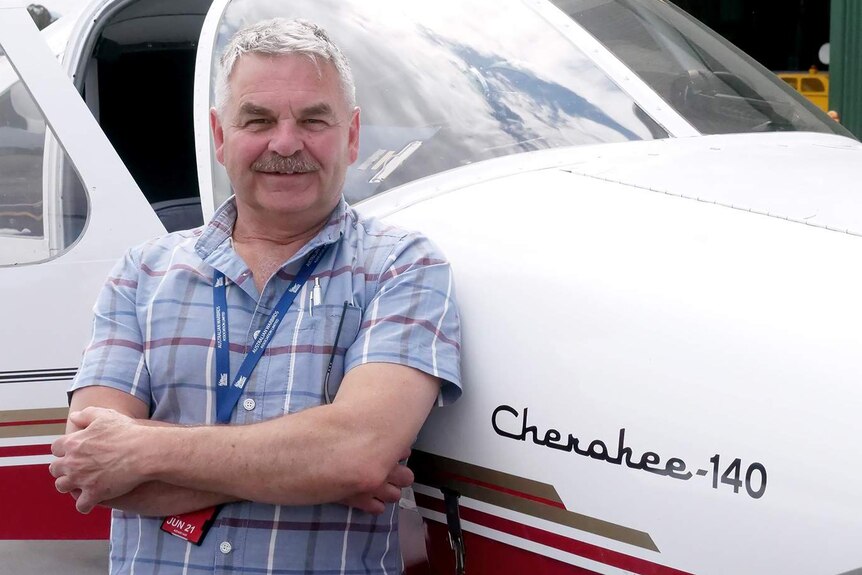 Mark Keech stands with arms folded in front of a small red and white plane.
