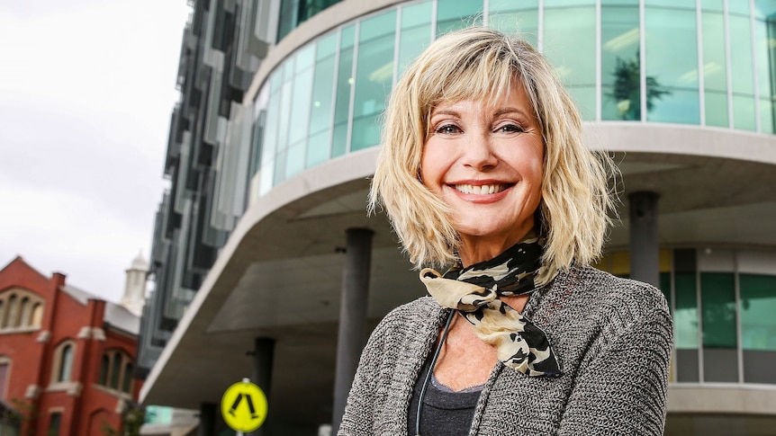 Olivia Newton-John stands smiling with her arms crossed out the front of the ONJ Centre.