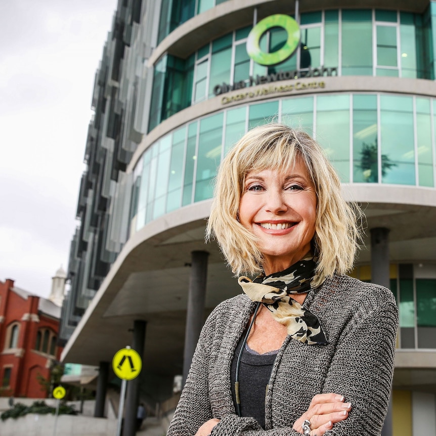 Olivia Newton-John stands smiling with her arms crossed out the front of the ONJ Centre.
