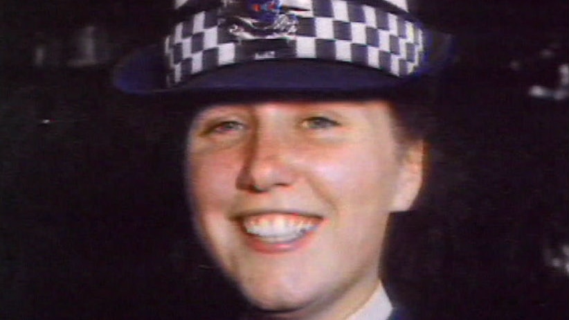 Angela Taylor wears a police uniform and hat.
