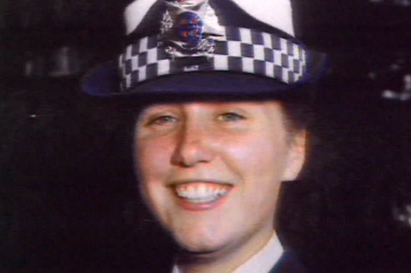 Angela Taylor wears a police uniform and hat.