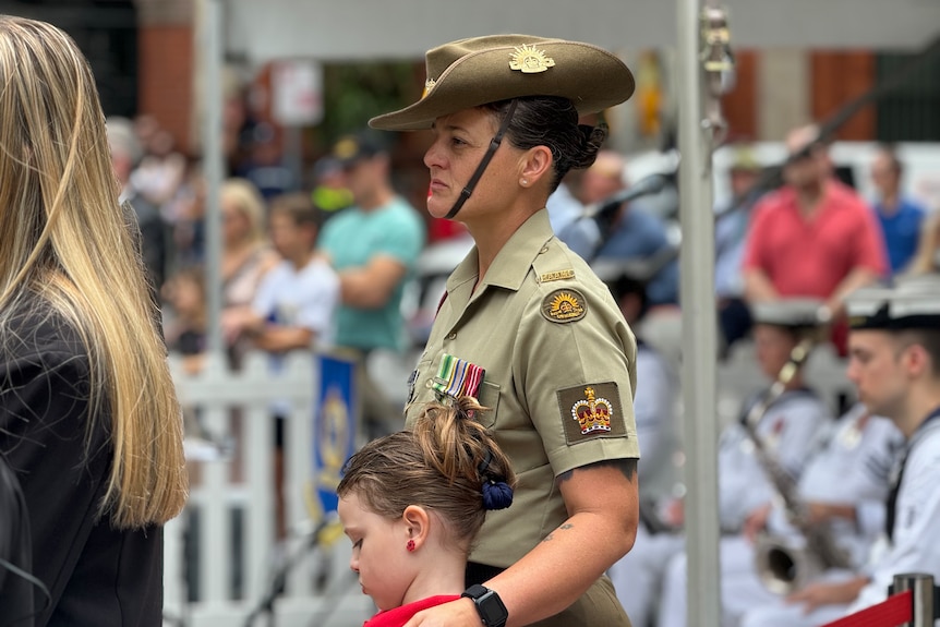 A servicewoman in uniform stands with a young girl.