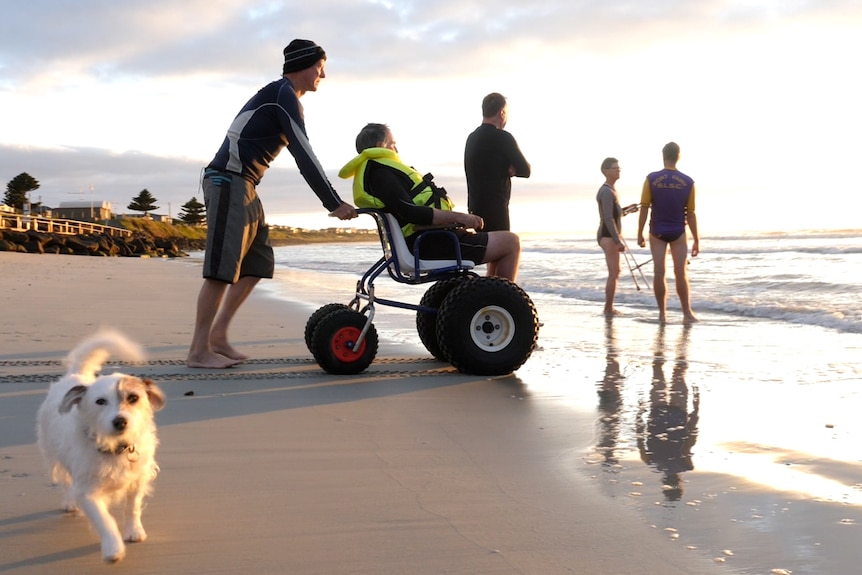 Man in wheel chair being pushed into ocean