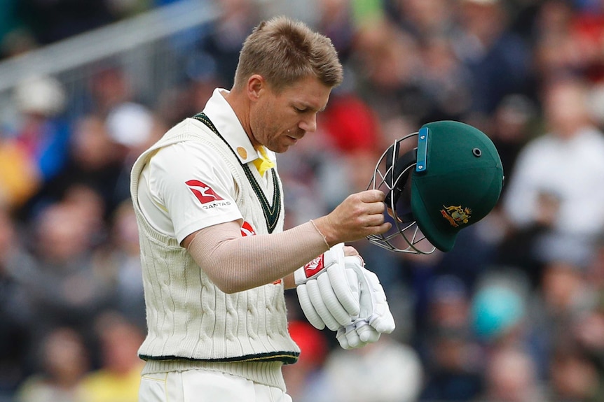 David Warner looks sadly at the ground as he takes his helmet off.