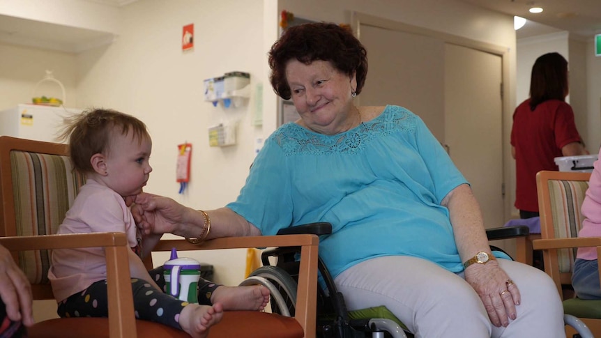 An older woman reaches her hand out to a toddler.