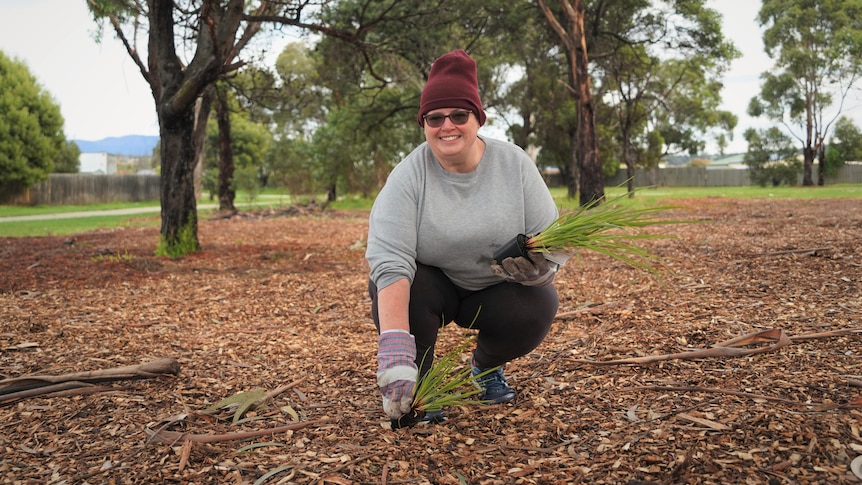 A woman in a beanie puts a grassy plant in a park