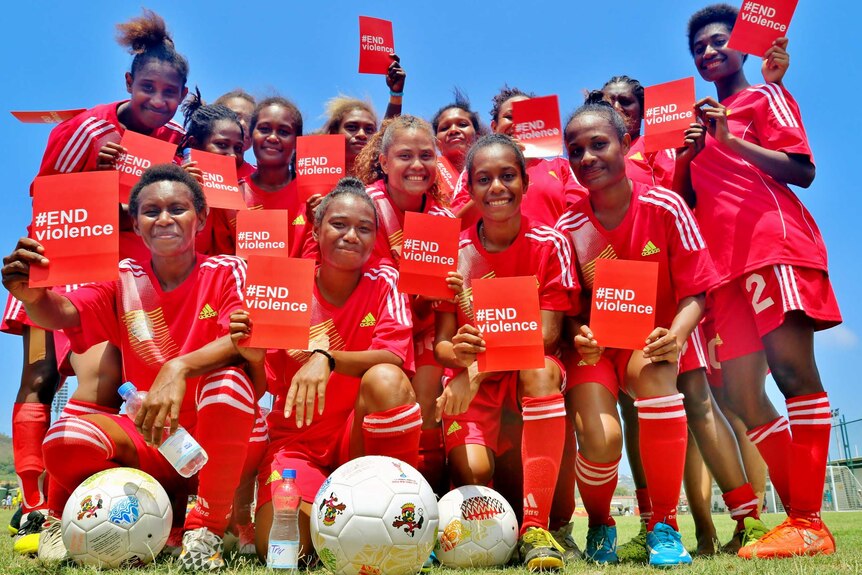 A Papua New Guinean women’s football team, wearing a red kit, hold up red cards with the words #ENDViolence.
