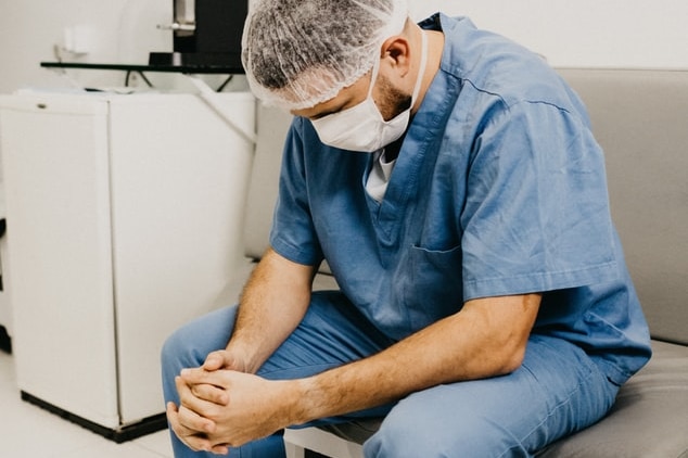 A doctor in scrubs looks at the floor.