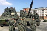 Men in fatigues stand with weapons around two tanks. 