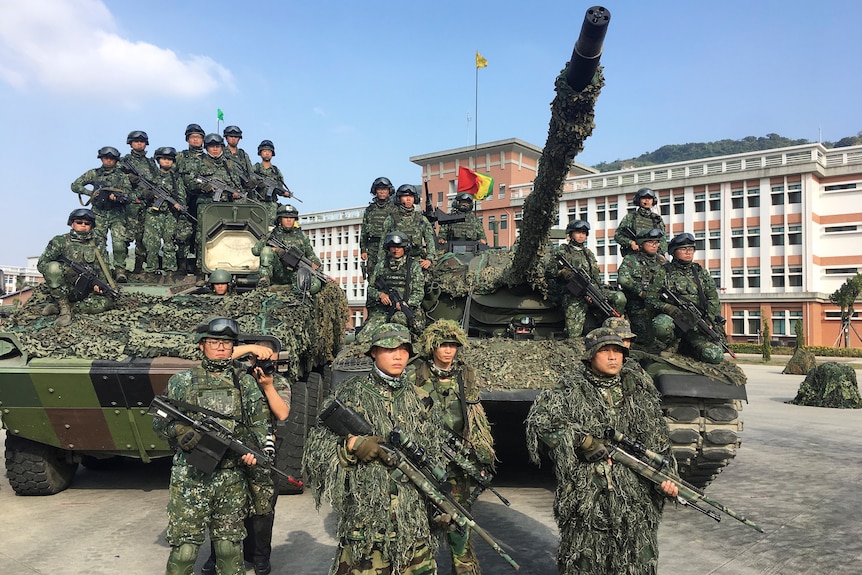 Men in fatigues stand with weapons around two tanks. 