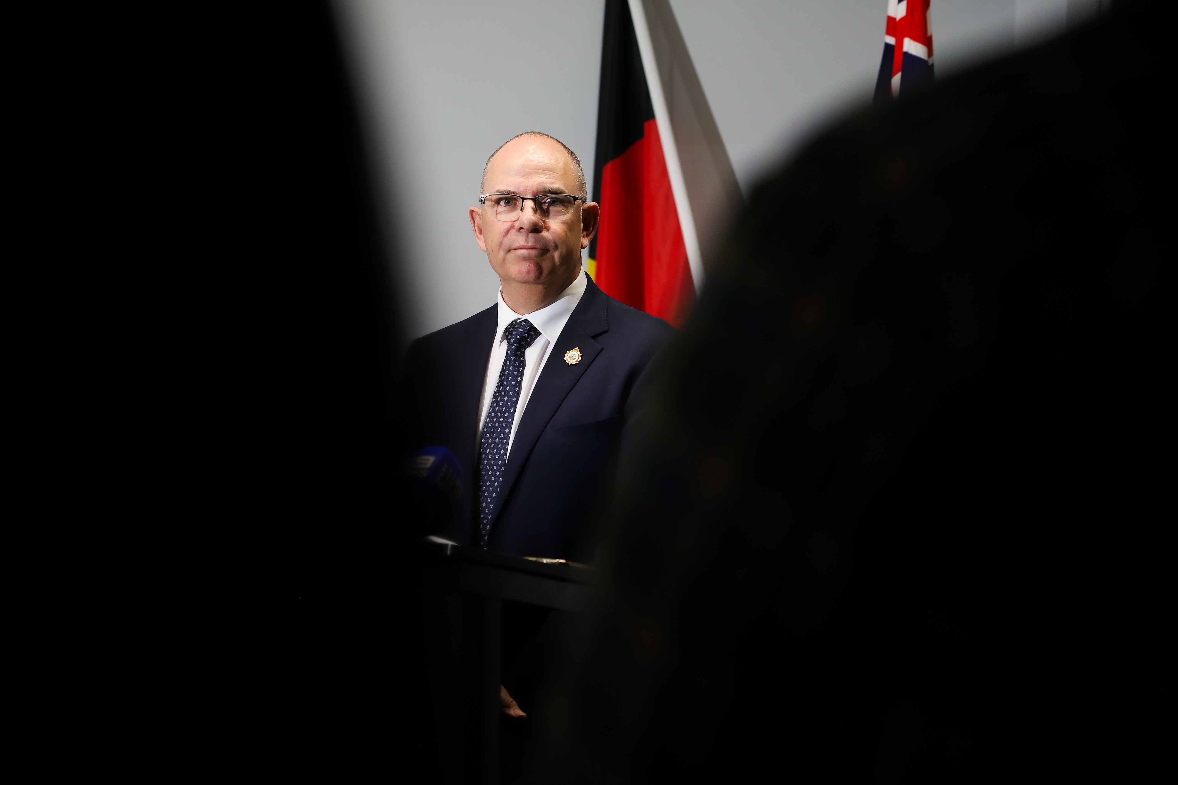 A long shot of a suited bald man wearing a pair of glasses.