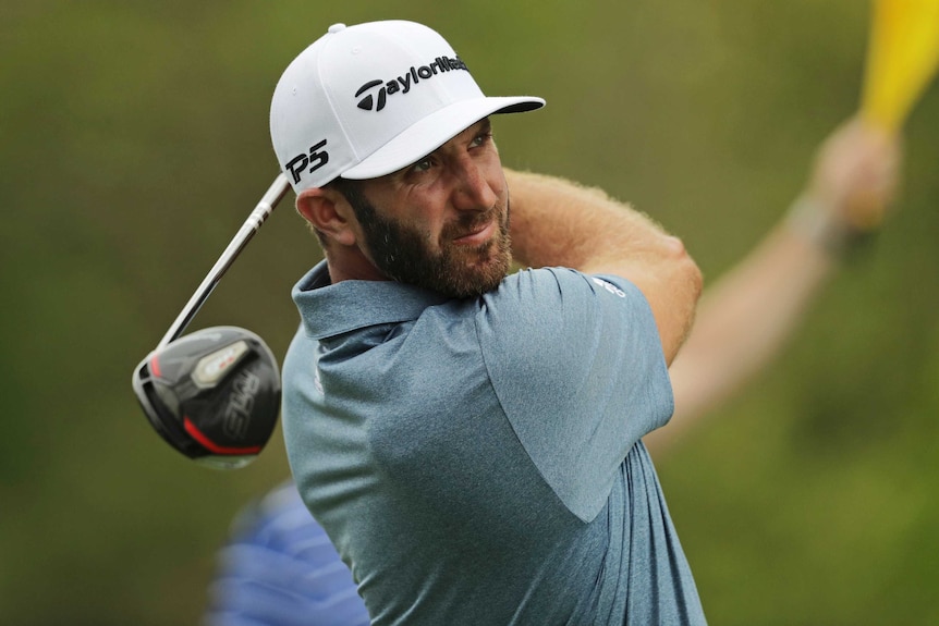 Duston Johnson looks at the ball with his golf club behind him as he completes a shot