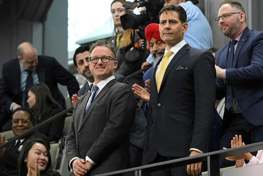 Two men in suits stand as the crowd applauds them. 