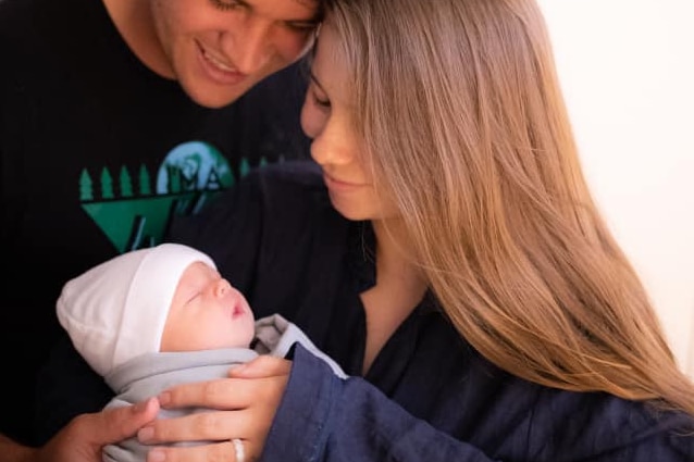 Young couple - man and woman - smiling as they hold a newborn baby in their arms.