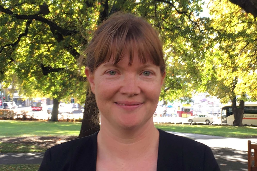 Sarah Lovell smiles and stands in front of trees.