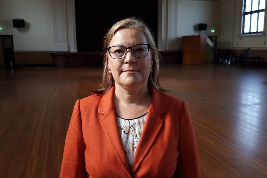 Woman in an orange jacket with glasses.