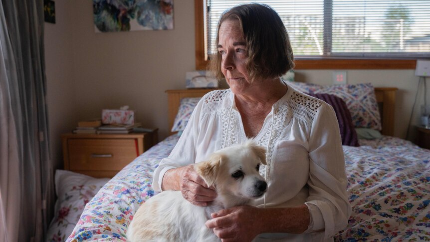 A woman sits on her bed with a dog on her lap.
