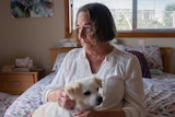A woman sits on her bed with a dog on her lap.