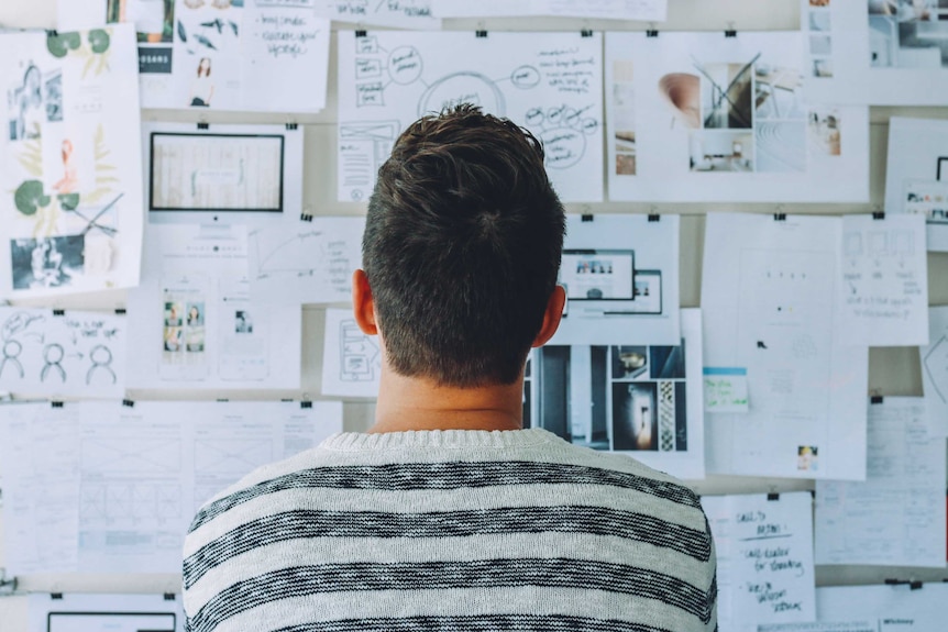 Man looking at a wall of papers and considering his options to depict a story about how to be better at making decisions.